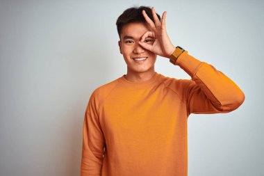 Genç Asya Çinli adam giymek turuncu kazak ayakta üzerinde izole beyaz arka plan yapma ok jest ile el gülümseyen, göz görünümlü parmaklar ile mutlu yüz.