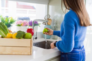 Genç kadın lavabo su kullanarak sebze ve meyve yıkama