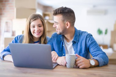 Genç çift bir kahve içme rahatlatıcı ve karton kutular etrafında bilgisayar laptop kullanarak, çok mutlu yeni bir eve hareket
