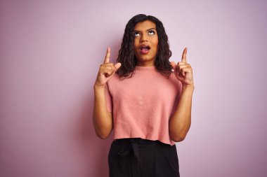 İzole pembe arka plan üzerinde genç güzel transseksüel transeksüel zarif kadın hayret ve görünümlü ve parmaklar ve yükseltilmiş kollar ile işaret şaşırttı.