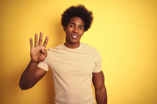 American man with afro hair wearing striped t-shirt standing over isolated yellow background showing and pointing up with fingers number four while smiling confident and happy.