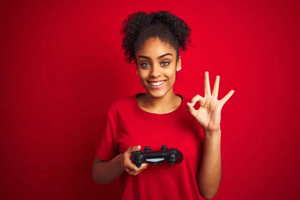 非洲裔美国玩家妇女玩视频游戏使用操纵杆在孤立的红色背景做确定标志用手指 优秀的符号 — 图库照片