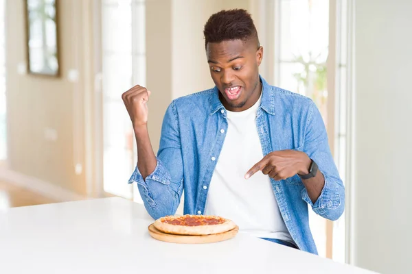 Africano Americano Homem Comendo Pizza Pepperoni Casa Muito Feliz Apontando — Fotografia de Stock
