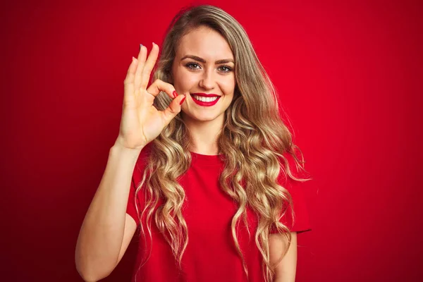 赤い孤立した背景の上に立つ基本的なTシャツを着た若い美しい女性は 手と指でOkサインをやって肯定的に微笑んでいます 成功した式 — ストック写真