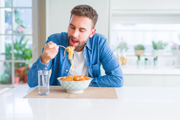 Charmant homme mangeant des pâtes avec des boulettes de viande et de la sauce tomate à hom — Photo