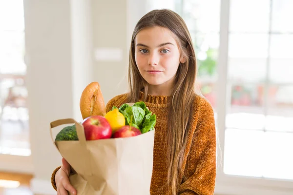 美しい女の子が新鮮な食料品の紙袋を持っている スマートな顔に自信を持って表現する真剣な考え — ストック写真