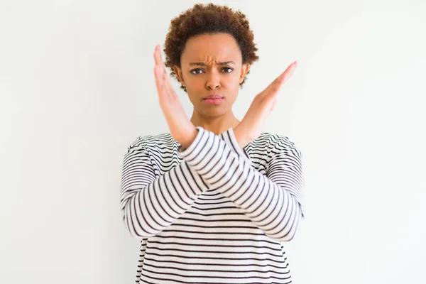 白い背景の上にストライプセーターを着た若い美しいアフリカ系アメリカ人女性は 否定的なサインをする腕を横切る表情を拒絶し 怒った顔 — ストック写真