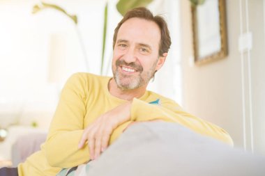 Rahat ve evde kameraya gülümseyen kanepede oturan yakışıklı orta yaş adam