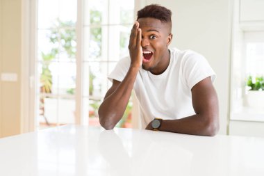 Evde beyaz masada yakışıklı Afrikalı Amerikalı adam yüz ve sürpriz duygu kendine güvenen gülümseme ile el ile bir göz kaplayan.