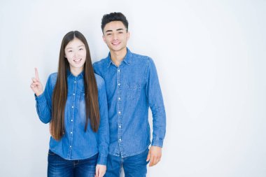 Beyaz izole arka plan üzerinde güzel genç Asya çift gösteren ve emin ve mutlu gülümseyen iken parmak numarası bir ile işaret.