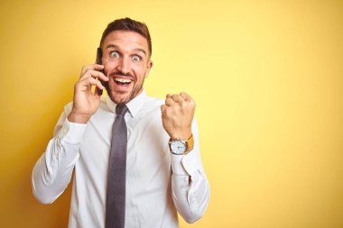 Genç yakışıklı iş adamı sarı izole arka plan üzerinde telefonda konuşurken gurur çığlık ve zafer ve başarı çok heyecanlı kutluyor, duygu tezahürat