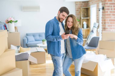 Genç çift karton kutular etrafında akıllı telefon kullanarak yeni bir eve hareket
