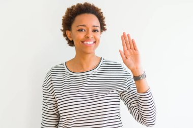 Beyaz arka planda çizgili kazak giyen genç güzel Afrikalı Amerikalı kadın Merhaba mutlu ve gülümseyen, dostça karşılama jest söyleyerek Waiving