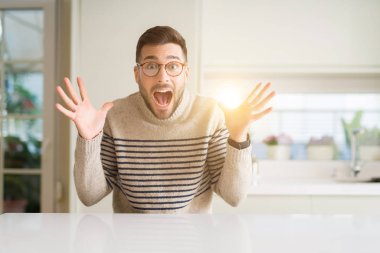 Evde gözlük giyen genç yakışıklı adam çılgın kutluyor ve başarı için hayran silah kaldırdı ve açık gözleri heyecanlı çığlık. Kazanan kavramı