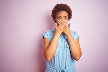 İzole pembe arka plan üzerinde afro saç ile genç güzel Afrikalı Amerikan kadın hata eller ile ağız kapsayan şok. Gizli konsept.