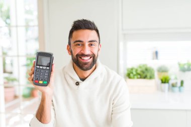Yakışıklı İspanyol adam tutmak noktası satış terminali dataphone ile mutlu bir yüz ayakta ve gülümseyen emin bir gülümseme ile diş gösteren