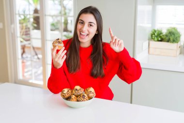 Çikolata cips yiyen güzel genç kadın bir fikir veya soru mutlu yüz, bir numara ile parmak işaret ile sürpriz Muffin