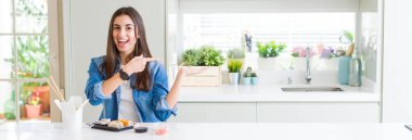 Güzel genç kadının geniş açı resmi teslim suşi yeme hayran ve kameraya gülümsüyor el ile sunmak ve parmak ile işaret ederken.