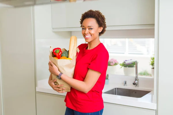 Young beautiful african american woman holding paper bag full of — Stock Photo, Image