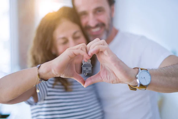 Middle age senior romantic couple holding and showing house keys, doing heart shape with hands smiling happy for moving to a new home