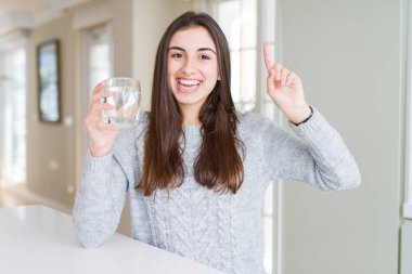Güzel genç kadın su taze bir bardak içme bir fikir veya soru mutlu yüz, bir numara ile parmak işaret ile şaşırdı