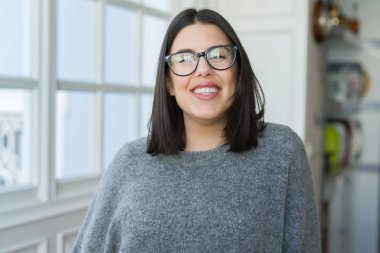 Güneşli bir günde evde rahat duran neşeli gülümseyen gözlüklü genç güzel kadın