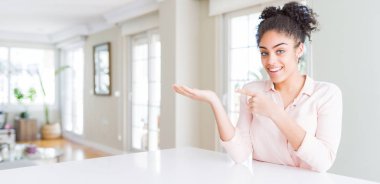 Afro saç ile güzel Afrikalı Amerikan kadın geniş açı hayran ve kamera gülümseyen el ile sunmak ve parmak ile işaret ederken.