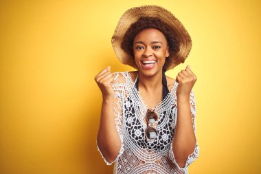 Afro saç ile genç Afrikalı Amerikan kadın beyaz izole arka plan üzerinde yaz şapka giyiyor şaşırttı ve silah yükseltilmiş ve açık gözleri ile başarı için hayran kutluyor. Kazanan kavramı.