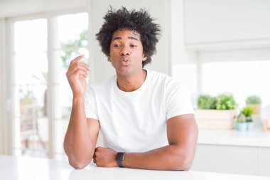 Genç afro-amerikan adam rahat beyaz t-shirt giyen evde oturan kamera hava güzel ve seksi olmak bir öpücük üfleme bakarak. Aşk ifadesi.