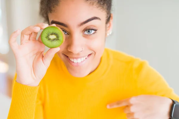 若いアフリカ系アメリカ人の女の子が自分に指を指して驚きの顔で緑のキウイを食べる — ストック写真