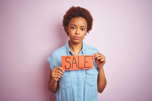 真剣に考えるスマートな顔に自信のある表情でピンクの孤立した背景の上に販売ボードを保持するアフリカ系アメリカ人女性 — ストック写真