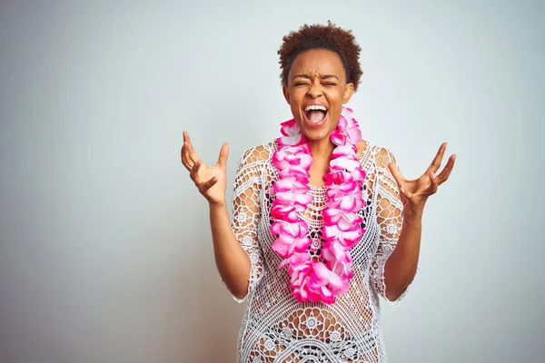 Young african american woman with afro hair wearing flower hawaiian lei over isolated background crazy and mad shouting and yelling with aggressive expression and arms raised. Frustration concept.