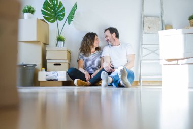 Orta yaş üst düzey romantik çift etrafında karton kutular ile daire katında oturan ve yeni bir eve taşınmak için mutlu gülümseyen aşk