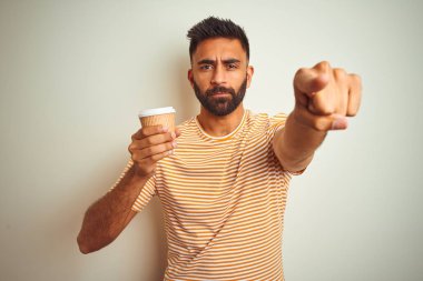 Genç Hint adam içme fincan kahve ayakta izole beyaz arka plan üzerinde parmak ile kamera ve size, el işareti, pozitif ve emin jest ön