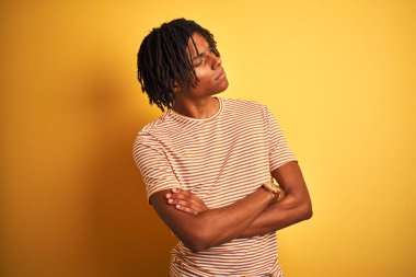 Sarı arka plan üzerinde duran çizgili t-shirt ayakta giyen dreadlocks ile Afro adam silah ile yan bakarak ikna ve emin geçti