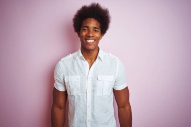 Afro saç ile genç Amerikan adam yüz üzerinde mutlu ve serin bir gülümseme ile izole pembe arka plan üzerinde ayakta beyaz gömlek giyiyor. Şanslı kişi.