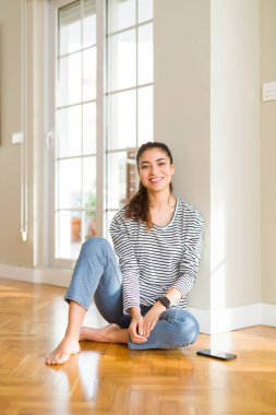 Genç güzel kadın yüzünde mutlu ve serin bir gülümseme ile evde yerde oturuyor. Şanslı kişi.