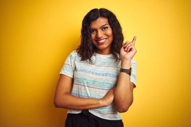 Yüzünde büyük bir gülümseme ile izole sarı arka plan üzerinde t-shirt giyen güzel transseksüel transeksüel kadın, kamera bakarak yan el ve parmak ile işaret.