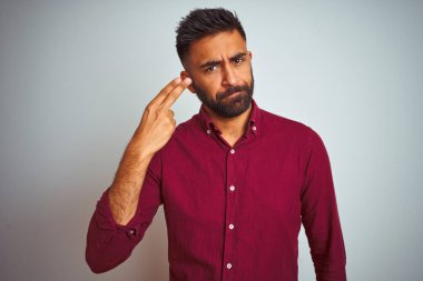 İzole gri arka plan üzerinde ayakta kırmızı zarif gömlek giyen genç Hintli adam ateş ve silah, intihar jest gibi baş el ve parmaklar işaret kendini öldürmek.