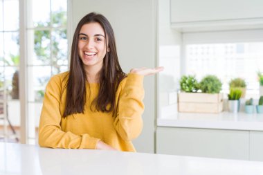 Sarı kazak giyen güzel genç kadın neşeli sunumu gülümseyen ve kamera bakarak el avuç ile işaret.