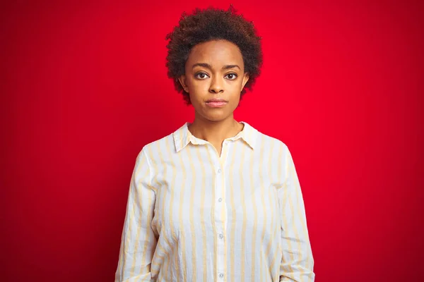 顔に真剣な表情を持つ孤立した赤い背景の上にアフロ髪を持つ若い美しいアフリカ系アメリカ人女性 カメラを見てシンプルで自然な — ストック写真