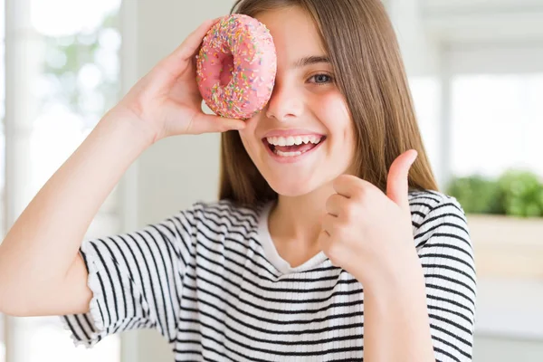 甘いピンクのドーナツを食べる美しい若い女の子の子供は Okサインをやって大きな笑顔で幸せ 指で親指アップ 優れた兆候 — ストック写真