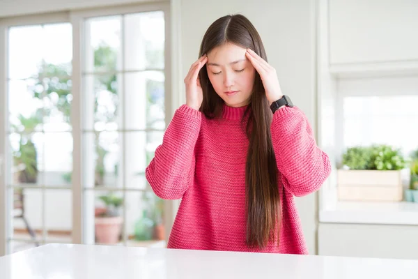 ストレスのため頭の痛みに頭を抱えた白いテーブルにピンクのセーターを着た美しいアジアの女性 苦しむ片頭痛 — ストック写真