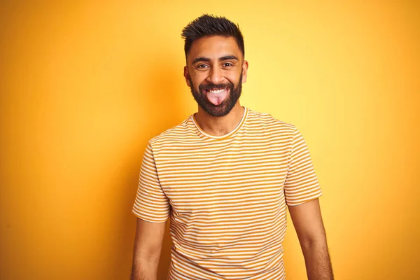孤立した黄色の背景の上に立つTシャツを着た若いインド人男性が おかしな表情で舌を突き出す 感情の概念 — ストック写真