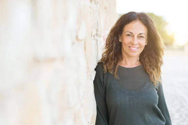 Hermosa mujer de mediana edad sonriendo alegre apoyado en un ladrillo w —  Fotos de Stock