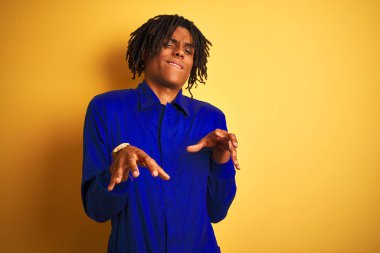 İzole sarı arka plan mide bulandırılmış ifade üzerinde mekanik üniforma giyen dreadlocks ile Afro işçi adam, hoşnutlu ve korkuyla nefretle yüz yapıyor çünkü kaçınma reaksiyon. Ellerle kaldırdı. Rahatsız edici kavramı.