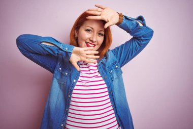Kot gömlek giyen güzel kızıl saçlı kadın ve izole pembe arka planda çizgili t-shirt gülümseyen neşeli oyun Peek bir Boo elleri ile yüz gösteren. Sürpriz ve çıkıldı