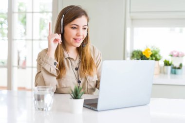 Güzel genç operatör kadın laptop ile çalışan ve kafa koltuğu giyen bir fikir veya soru mutlu yüz, bir numara ile parmak işaret şaşırttı