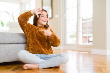Evde oturan güzel genç kız çocuk mutlu yüz ile eller ve parmaklar ile çerçeve yapma gülümseyen. Yaratıcılık ve Fotoğrafçılık konsepti.