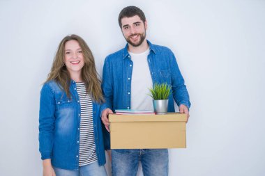 Genç çift ayakta mutlu bir yüz ile beyaz izole arka plan üzerinde yeni eve hareket karton kutu tutan ve dişleri gösteren kendinden emin bir gülümseme ile gülümseyerek